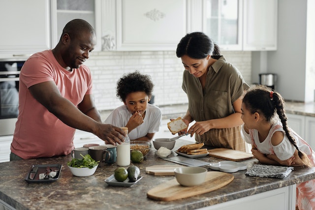 Two parents and their children prepare breakfast on a kitchen island with a granite countertop